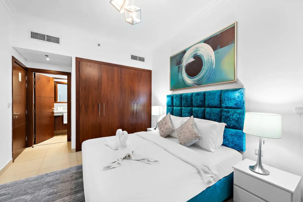 Un dormitorio con una cama blanca, un cabecero azul tapizado y una obra abstracta.