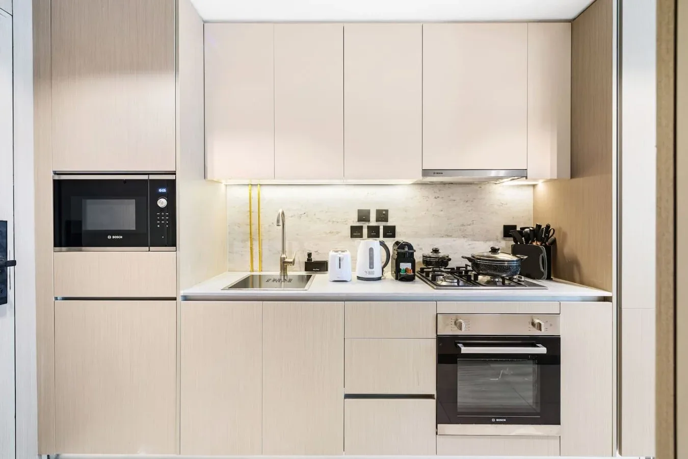 Una cocina moderna con gabinetes claros, una placa de cocina y electrodomésticos empotrados.