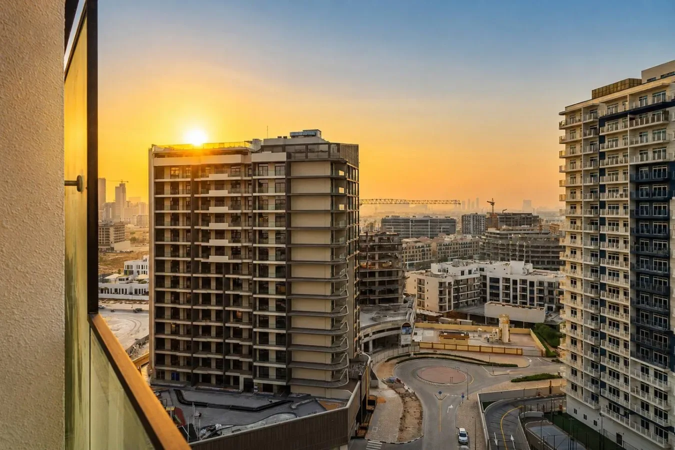 Vista de la ciudad al atardecer, con edificios altos y una grúa de construcción a lo lejos.