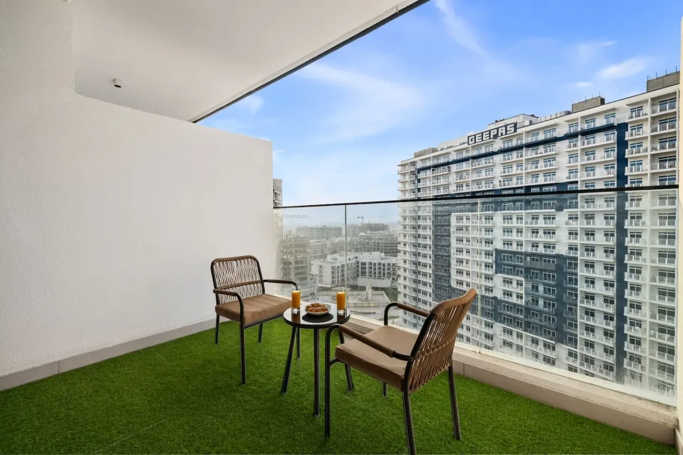 Una zona de estar en el balcón con una mesa pequeña da a edificios altos cercanos.