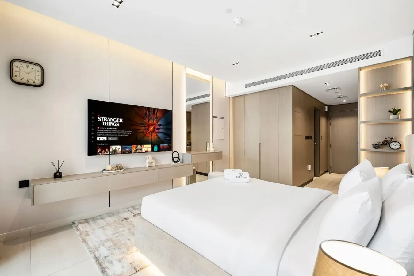 Un dormitorio luminoso con una cama grande, un televisor en la pared y estanterías empotradas.