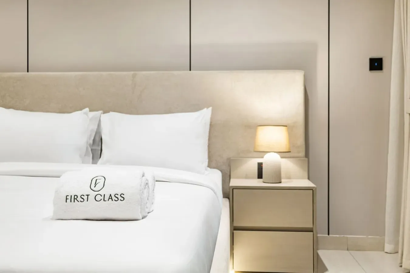 Una cama bien arreglada con ropa de cama blanca y una lámpara de noche.