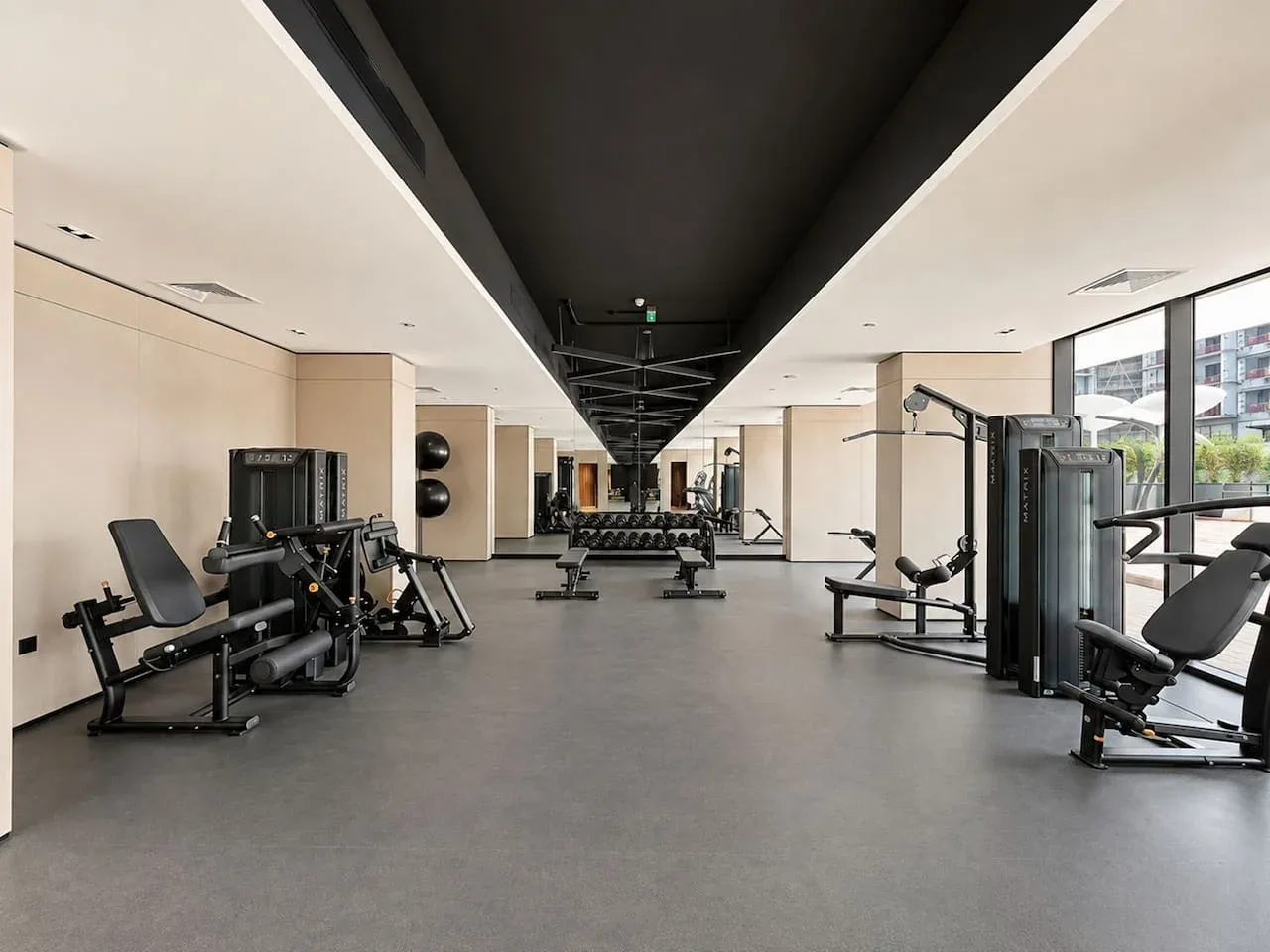 Un gimnasio amplio con máquinas de ejercicio y grandes ventanas.