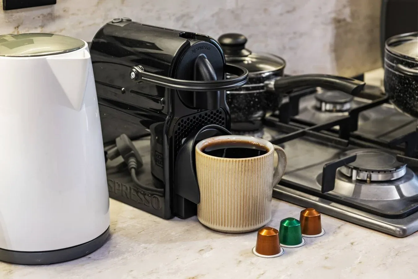 Una encimera de cocina con cafetera, taza y hervidor junto a una cocina de gas.