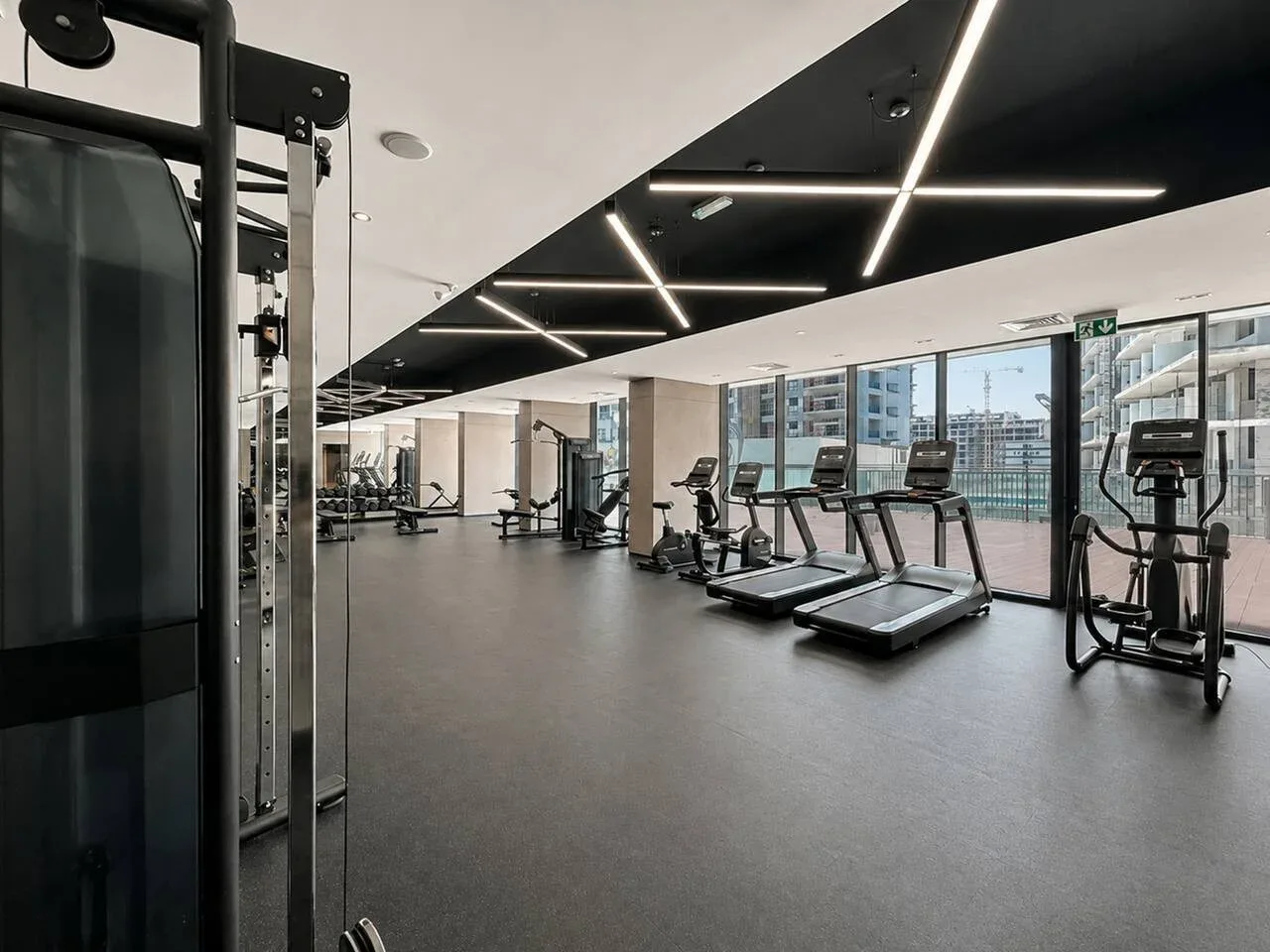 Un gimnasio con máquinas de ejercicio y cintas de correr junto a grandes ventanas.