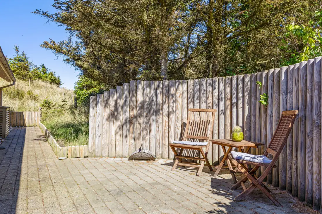 Un patio al aire libre con asientos de madera junto a una cerca alta y árboles.