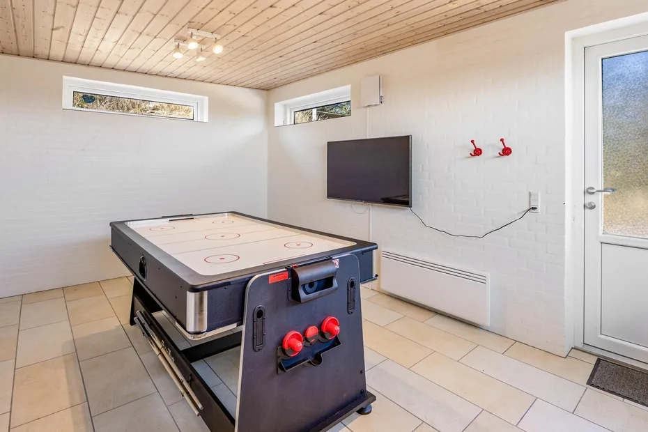 Una sala de recreación con una mesa de hockey de aire y un televisor en la pared.
