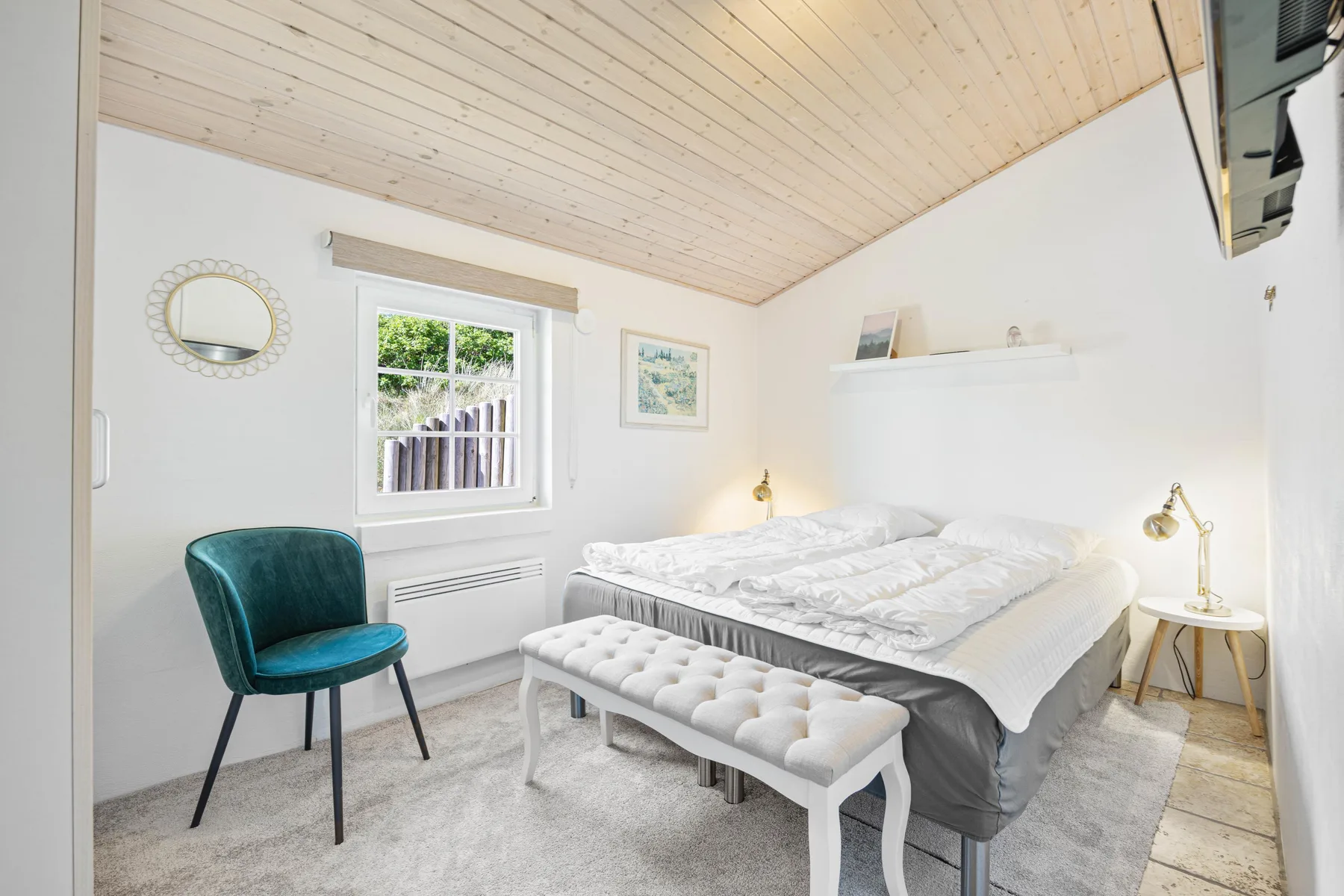 Un dormitorio luminoso con una cama doble, una silla verde azulado y un banco acolchado.