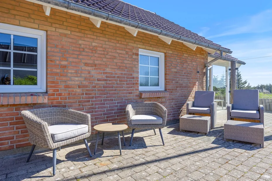 Un patio pavimentado junto a una casa de ladrillo tiene varios asientos y mesas pequeñas.
