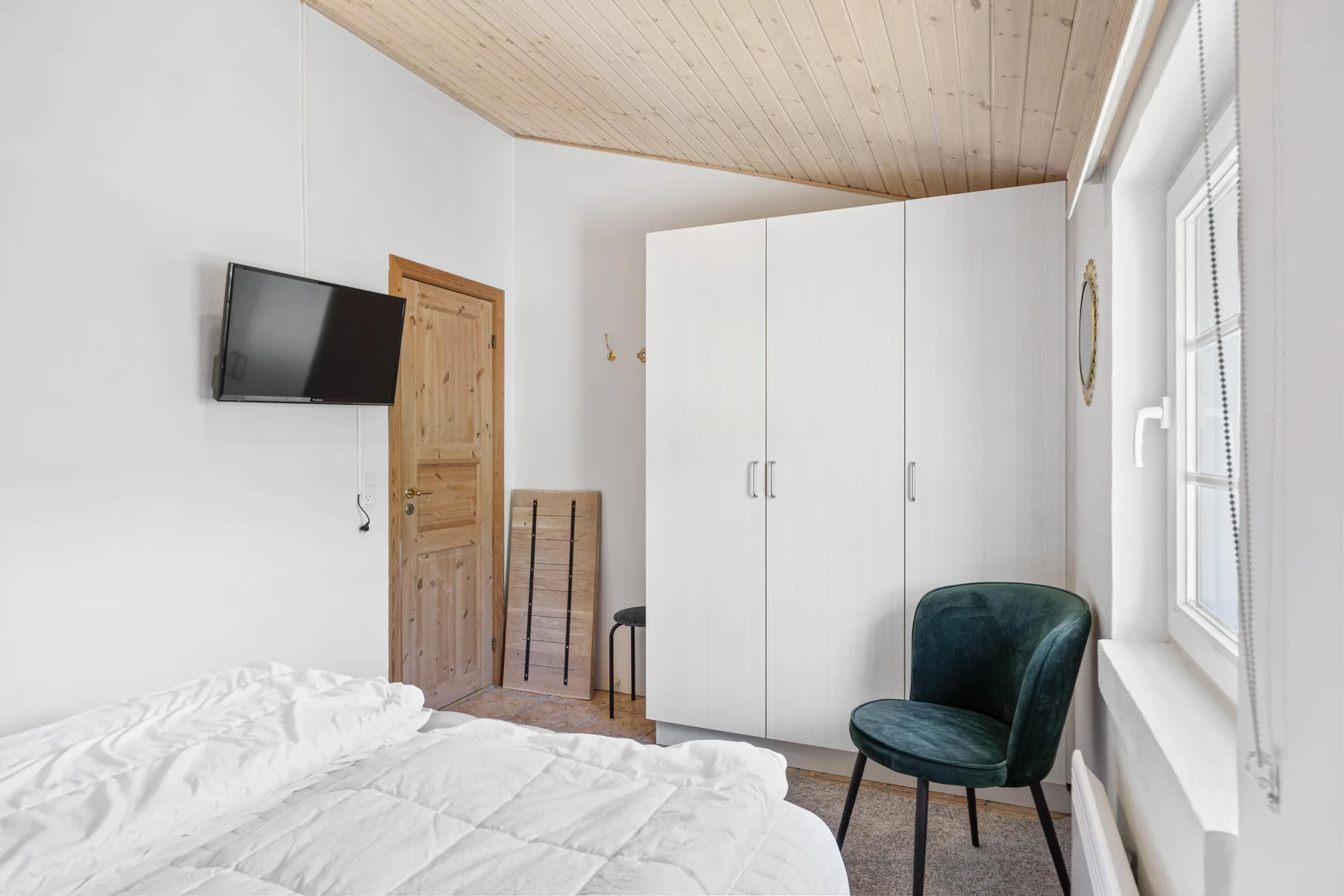 Un dormitorio luminoso con una cama, un armario blanco y un asiento tapizado verde.