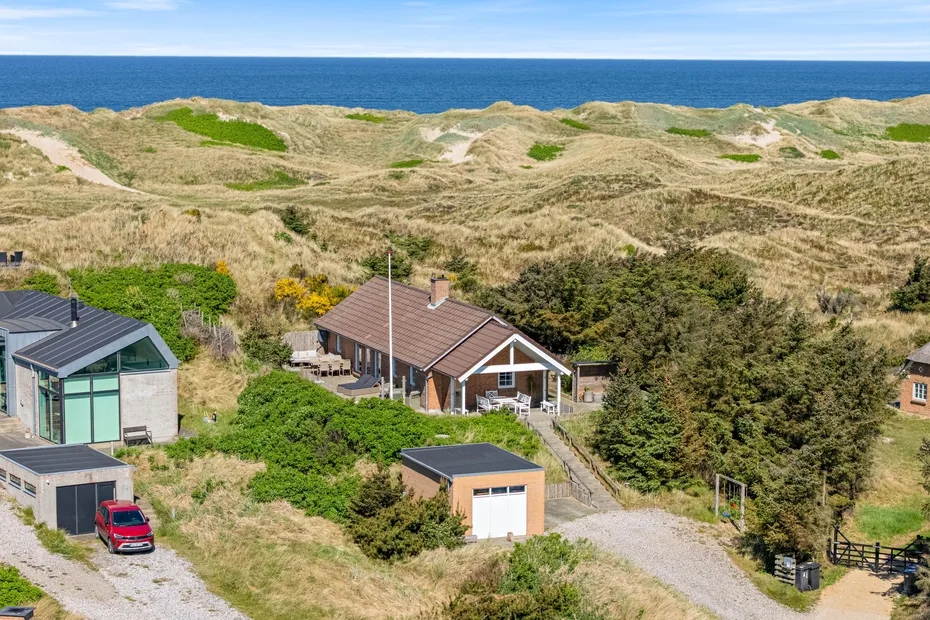 Casas entre dunas costeras, con el mar visible a lo lejos.