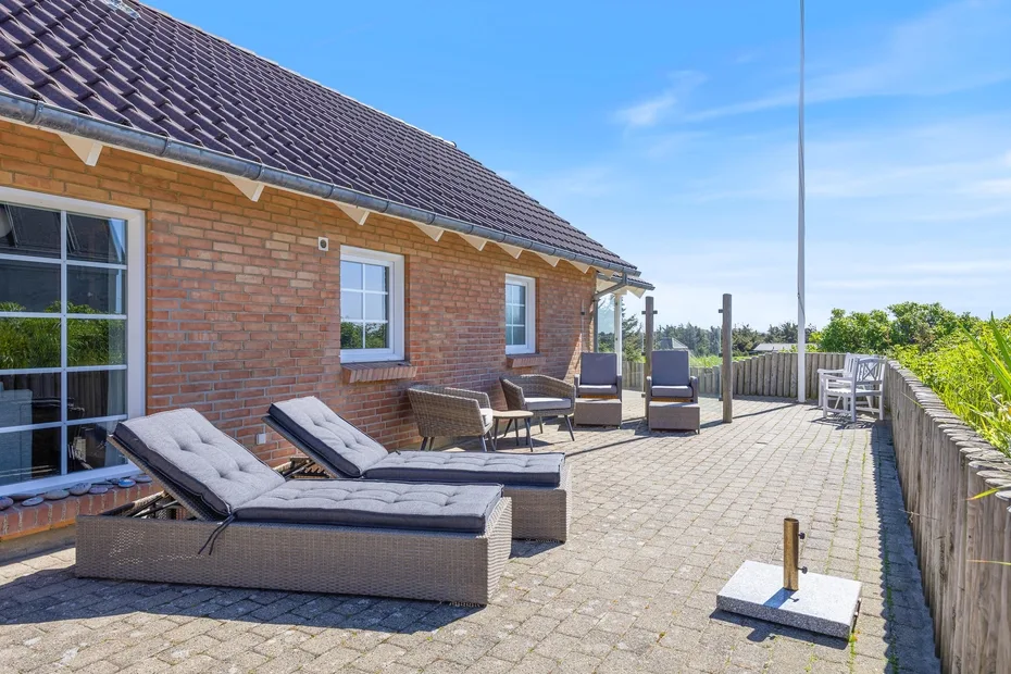 Un patio pavimentado junto a una casa de ladrillo tiene asientos de descanso y una zona para comer al aire libre.