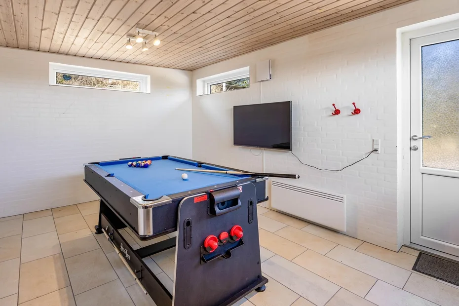 Una sala de juegos con una mesa de billar de paño azul y un televisor en la pared.