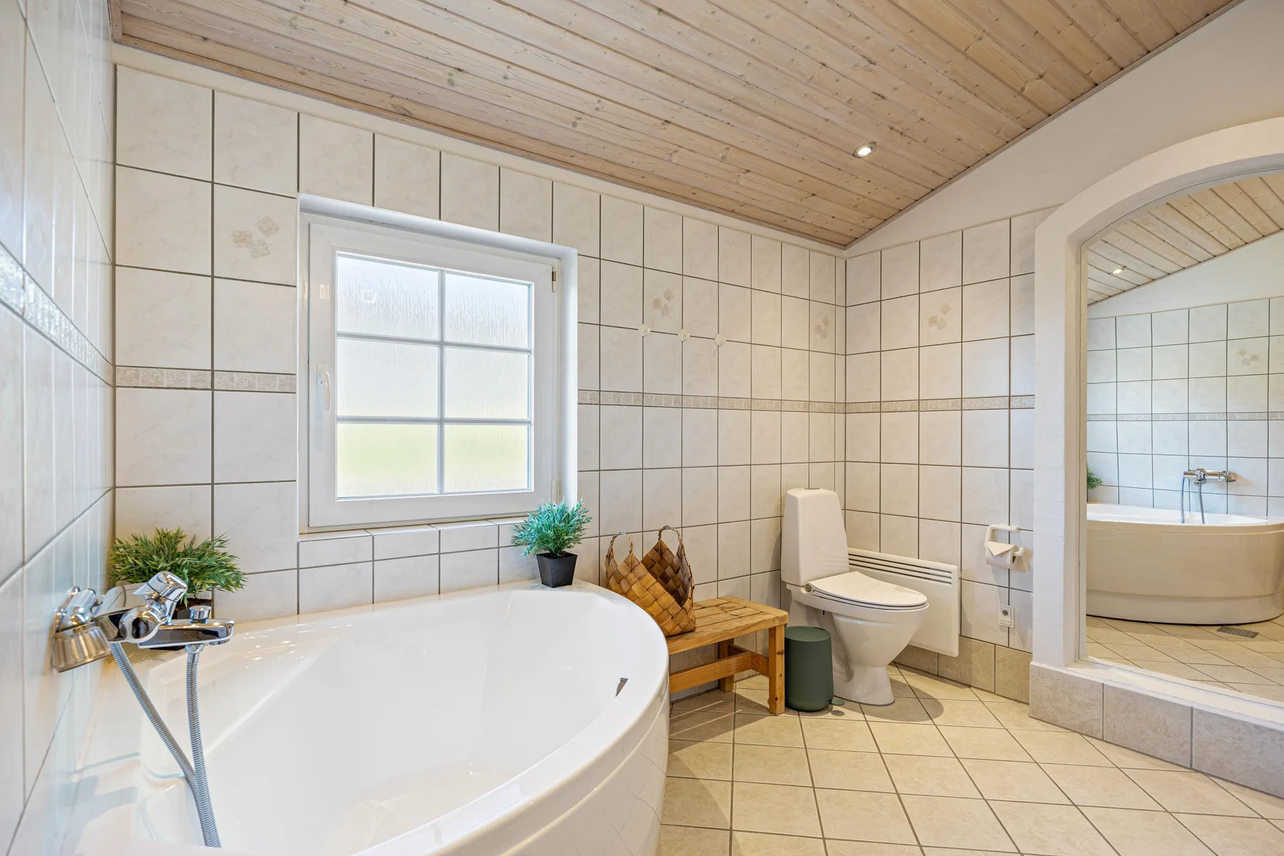 Un baño con azulejos, una bañera grande, un inodoro y una ventana.