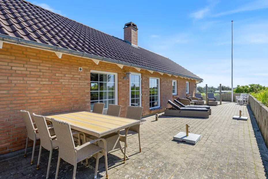 Un patio pavimentado junto a una casa de ladrillo tiene una mesa de comedor y asientos de descanso.