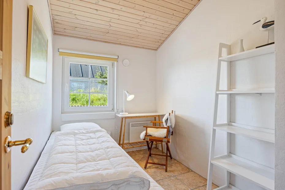 Un dormitorio luminoso con una cama individual, escritorio y ventana.