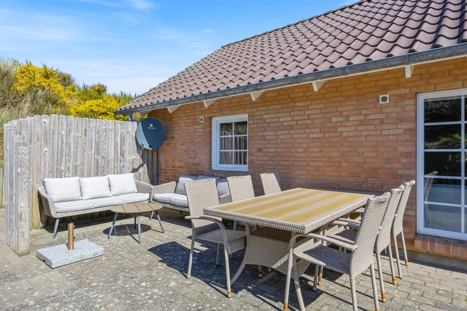 Un patio exterior pavimentado con mesa de comedor y asientos acolchados junto a una casa de ladrillo.
