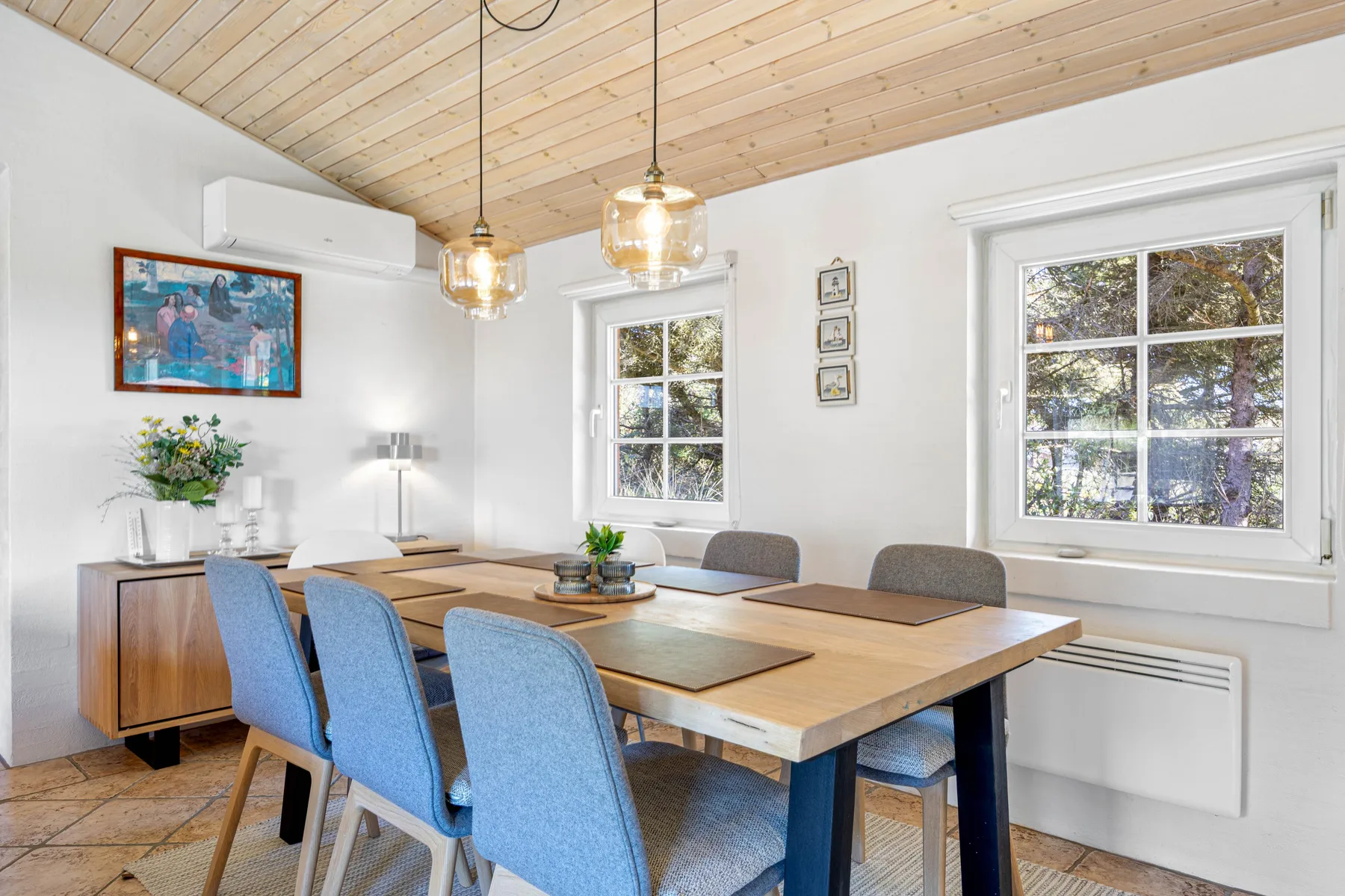 Un comedor con una mesa de madera, asientos azules y ventanas grandes.