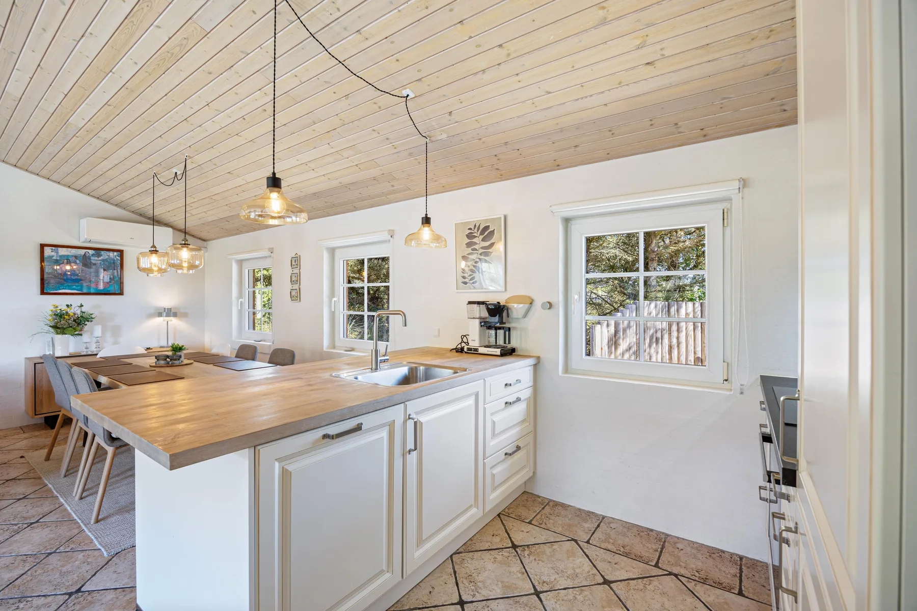 Una cocina luminosa con una isla grande, lámparas colgantes y ventanas.