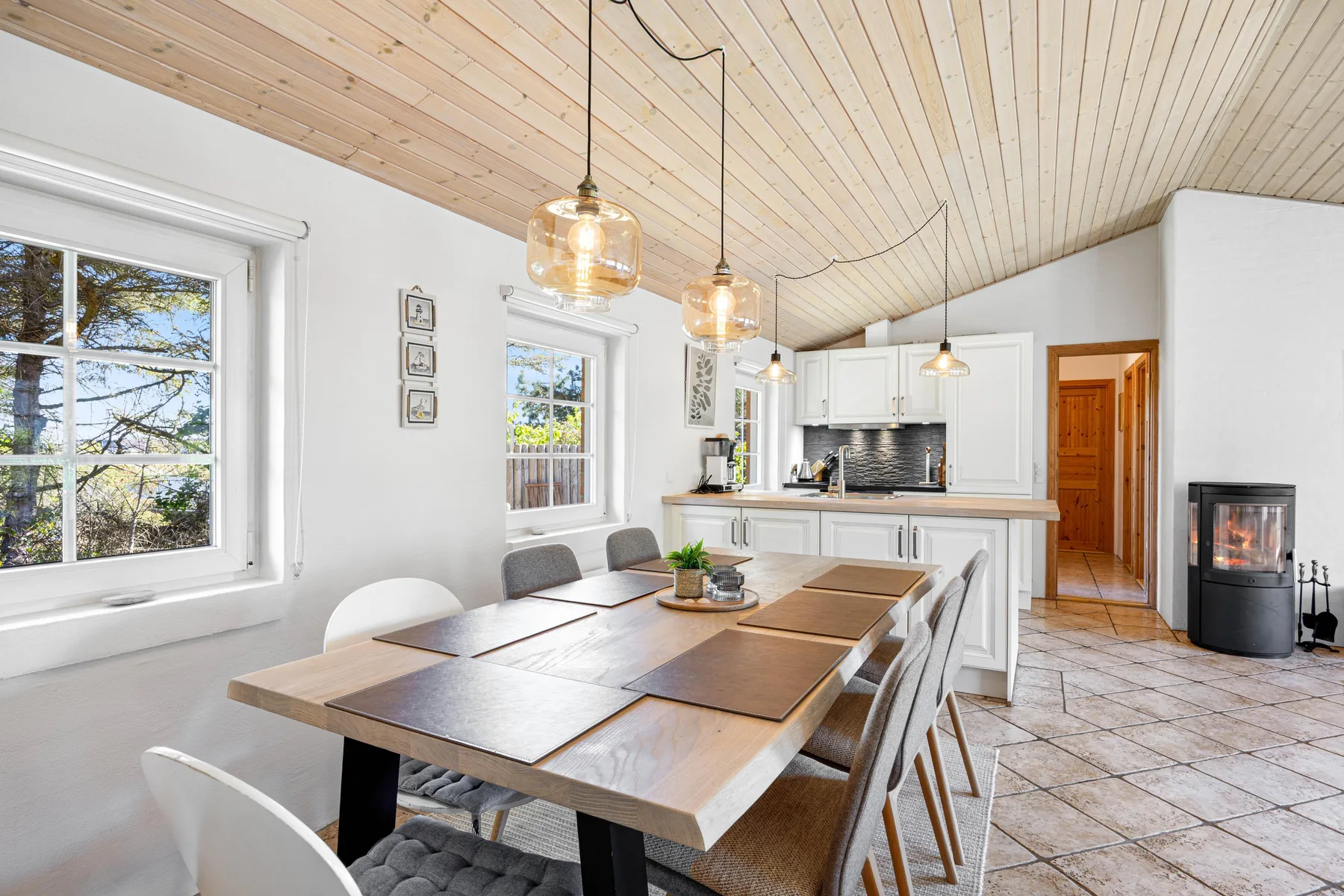 Un comedor luminoso se abre a una cocina blanca bajo un techo revestido de madera.