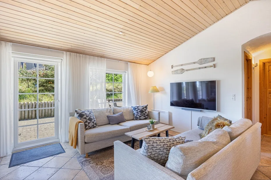 Una sala luminosa con asientos, un televisor y puertas de vidrio que dan a un patio.