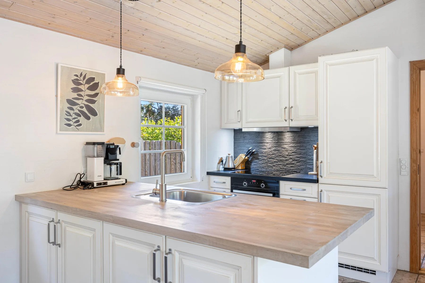 Una cocina luminosa con gabinetes blancos, una isla central y lámparas colgantes.