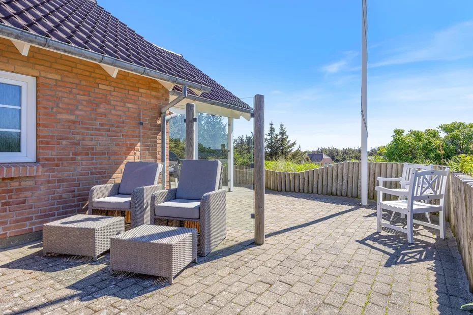 Un patio pavimentado junto a una casa de ladrillo, con asientos y una cerca de madera.