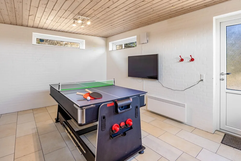 Una sala de recreo con una mesa de tenis de mesa y un televisor en la pared.