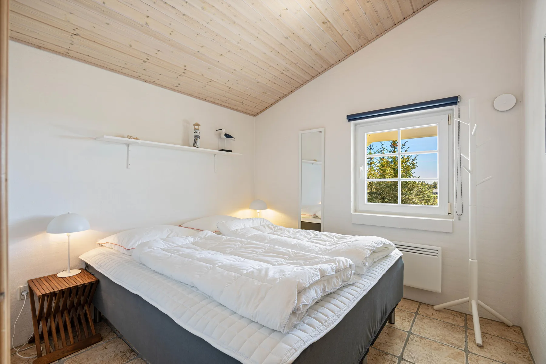Un dormitorio luminoso con una cama bajo un techo inclinado de madera.