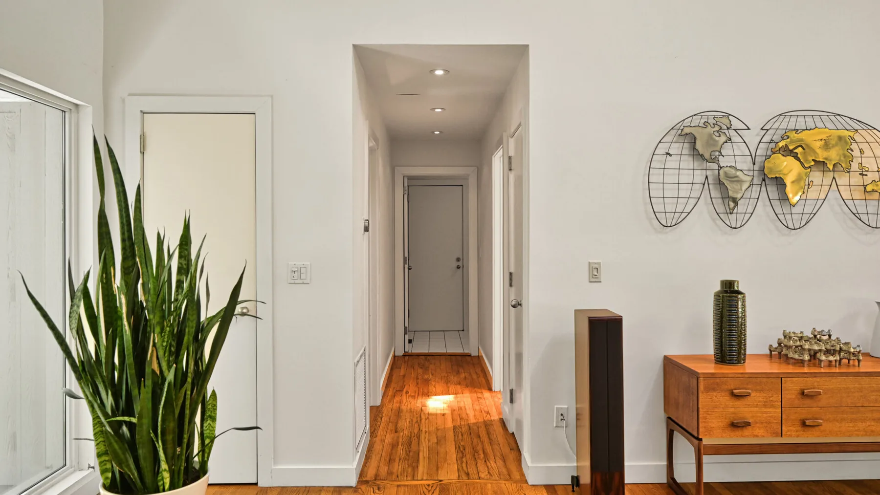 Un pasillo luminoso con suelo de madera, una consola y una planta en maceta.