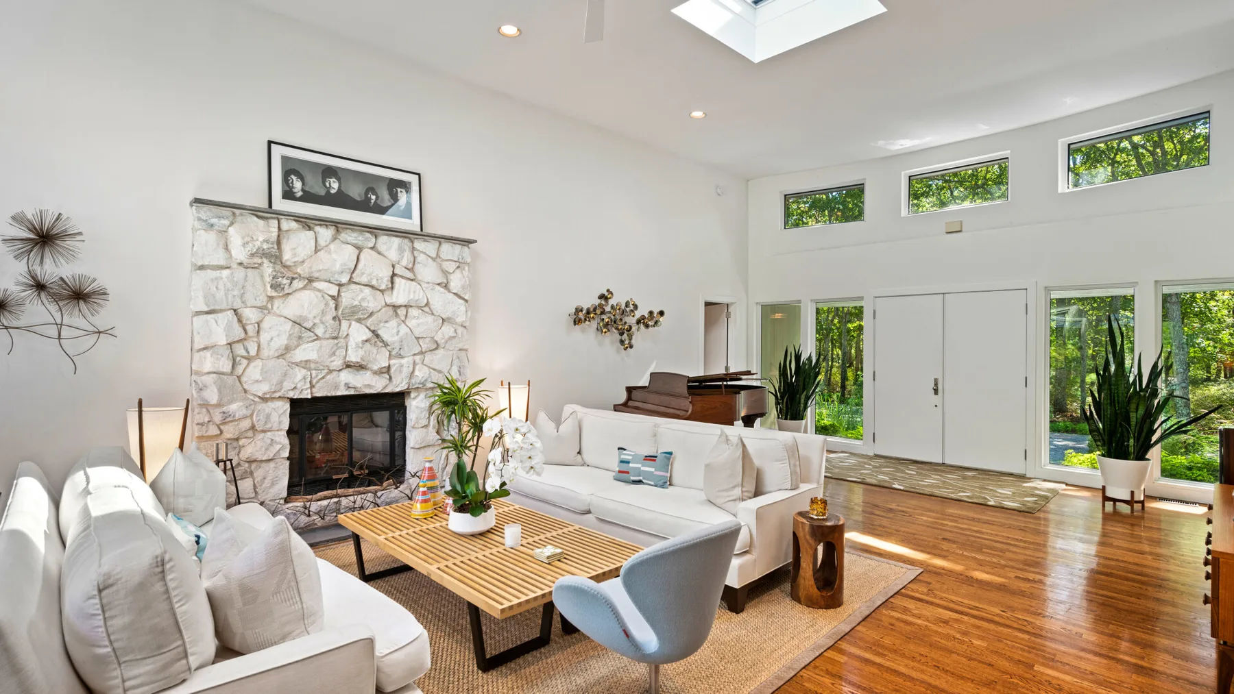 A bright living room with white seating, a stone fireplace, and large windows.