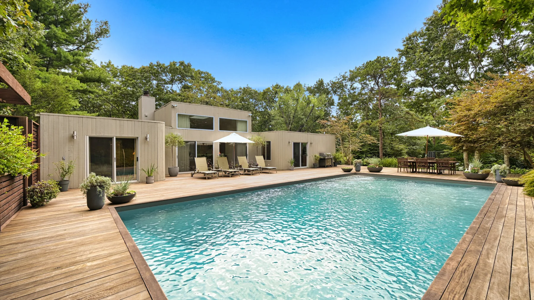 An outdoor swimming pool is surrounded by a wooden deck and leafy trees.