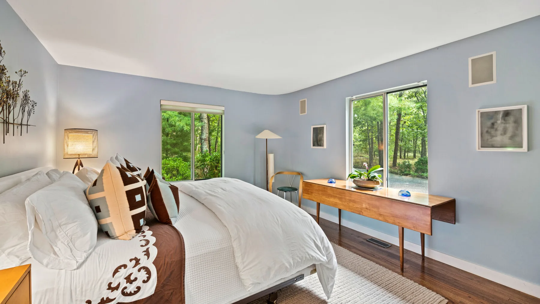 Un dormitorio luminoso con una cama bien tendida y ventanas con vistas a la vegetación.