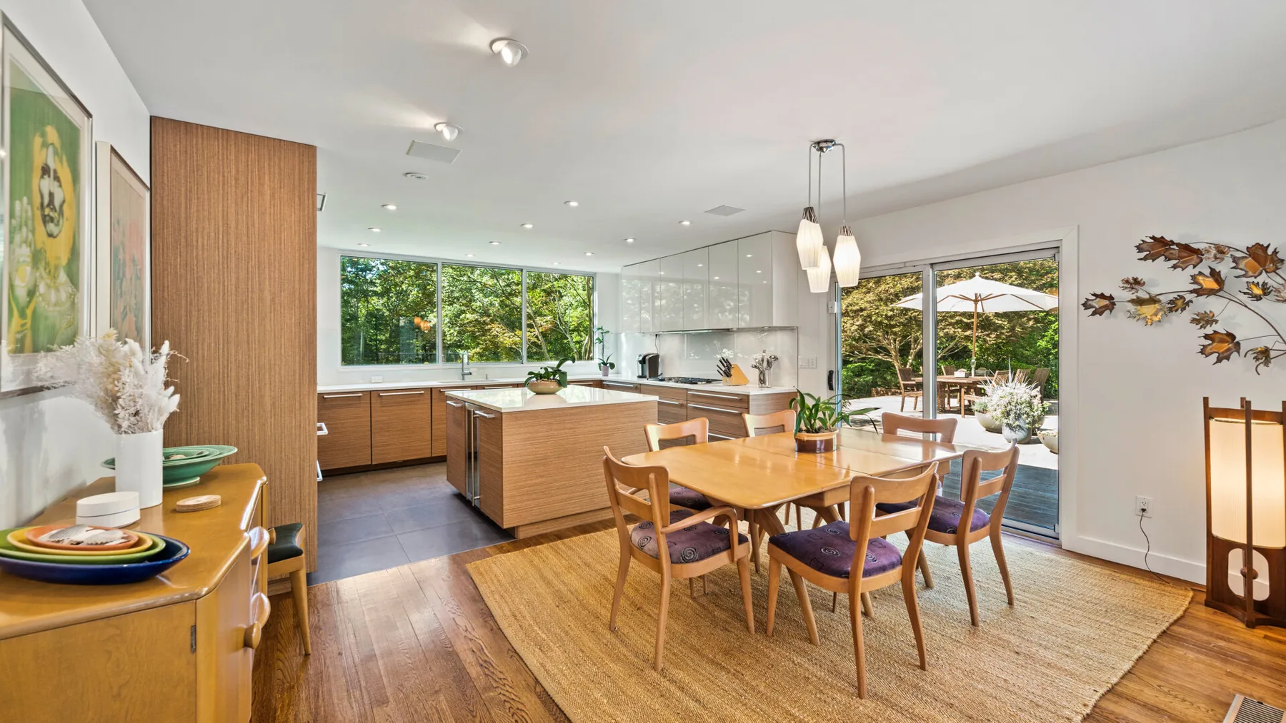 Una cocina abierta y zona de comedor con una mesa de madera junto a grandes ventanas.