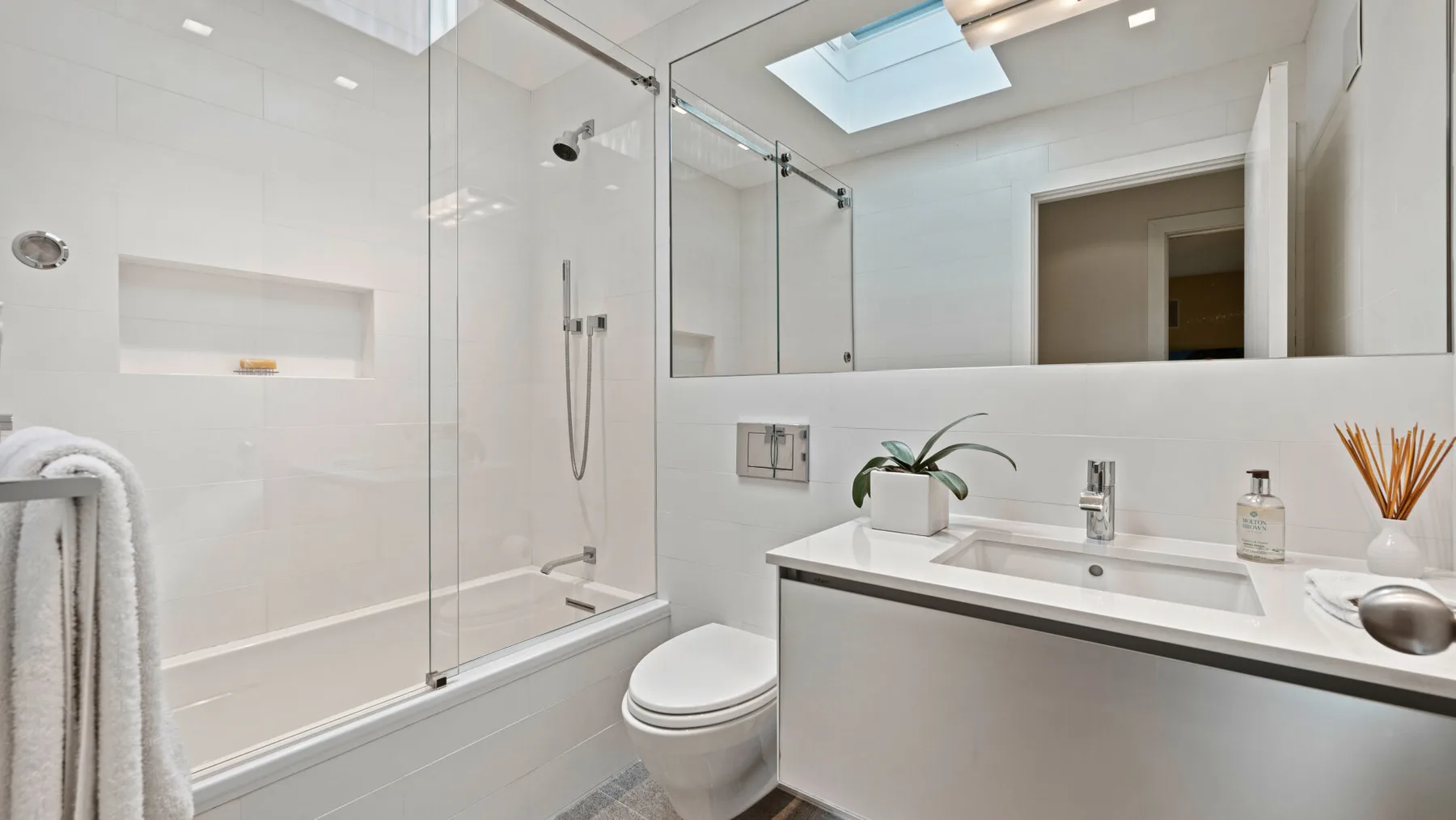 Un baño luminoso con ducha de vidrio, inodoro y lavabo bajo una claraboya.