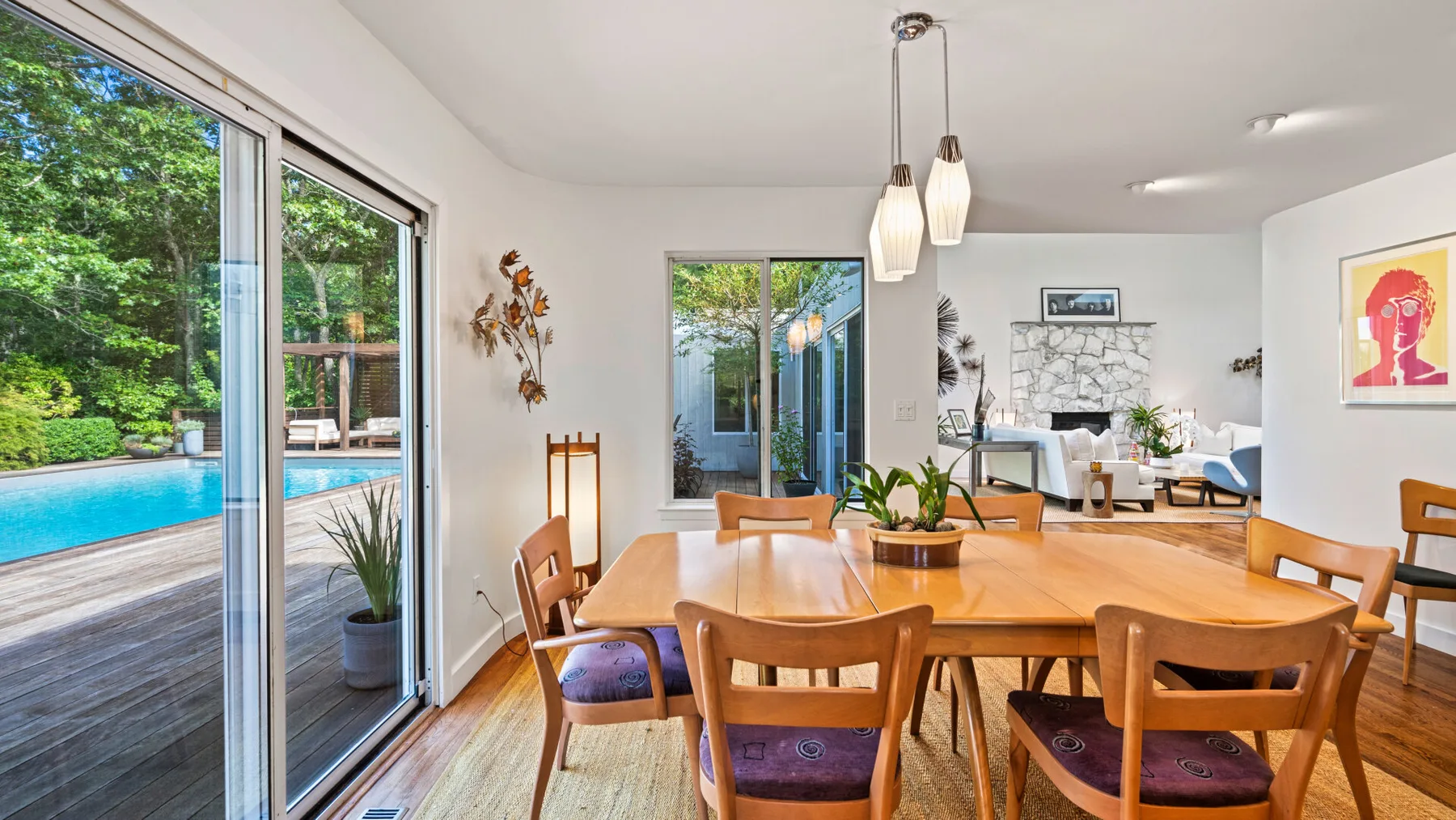 Comedor con mesa y sillas de madera junto a grandes ventanas con vistas a una piscina.