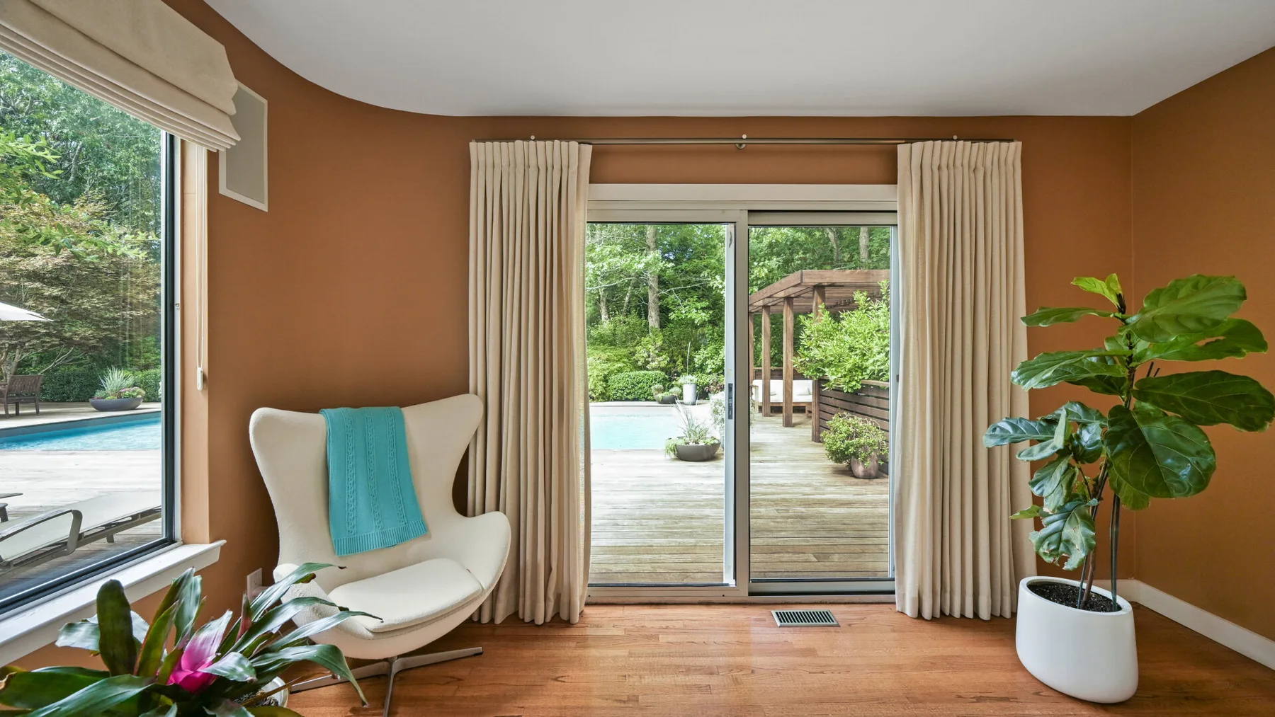 Una habitación luminosa da a una terraza mediante puertas corredizas de vidrio, con plantas junto a las ventanas.