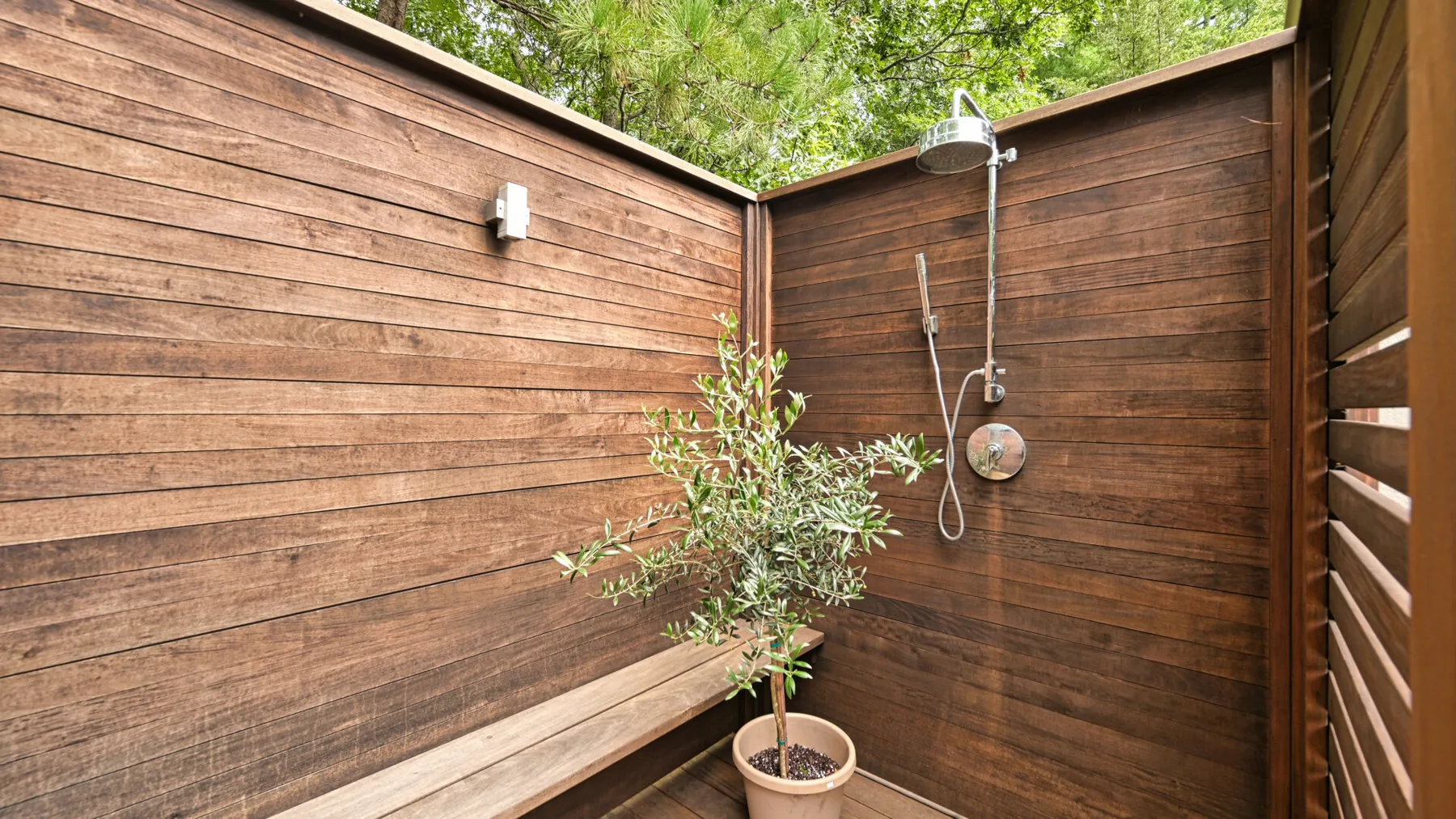 Una ducha exterior rodeada de paredes de madera, con una planta en maceta cerca.