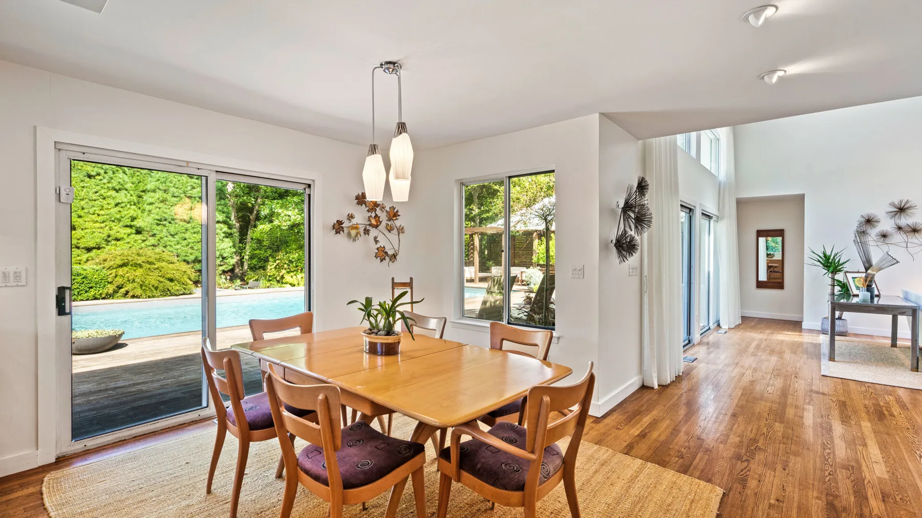 Un comedor luminoso se abre a un patio y una piscina mediante grandes puertas de vidrio.