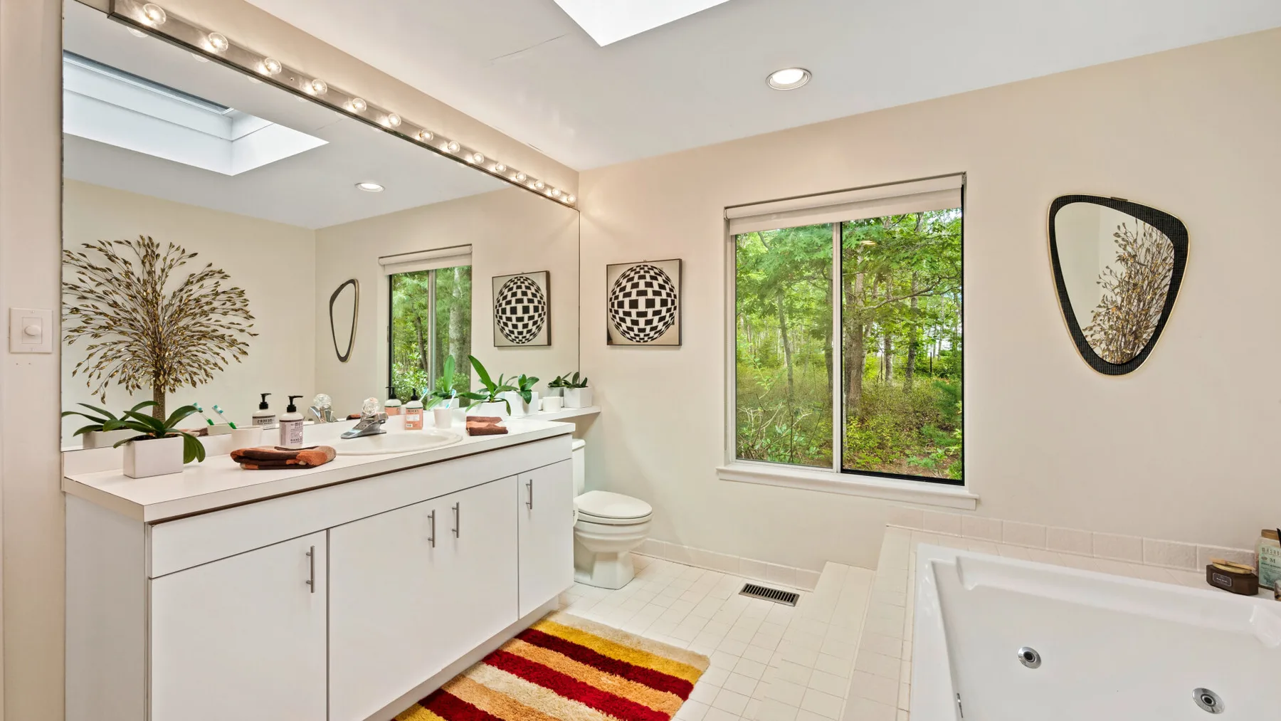 Un baño luminoso con un tocador largo, espejo y ventana con vista a la vegetación.