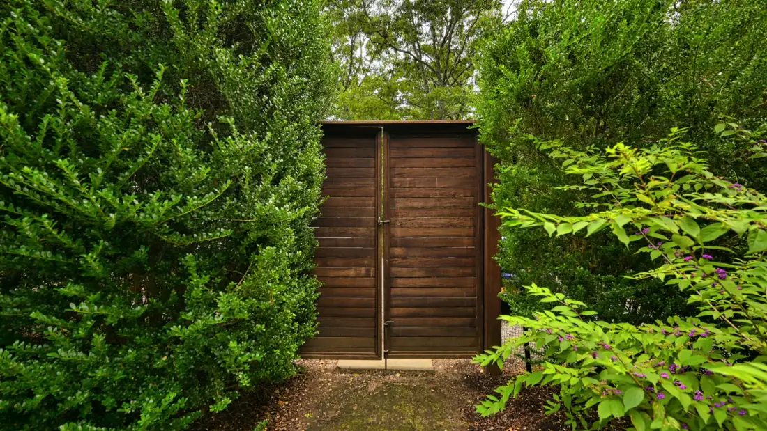 Una puerta de jardín de madera está entre arbustos verdes y frondosos.