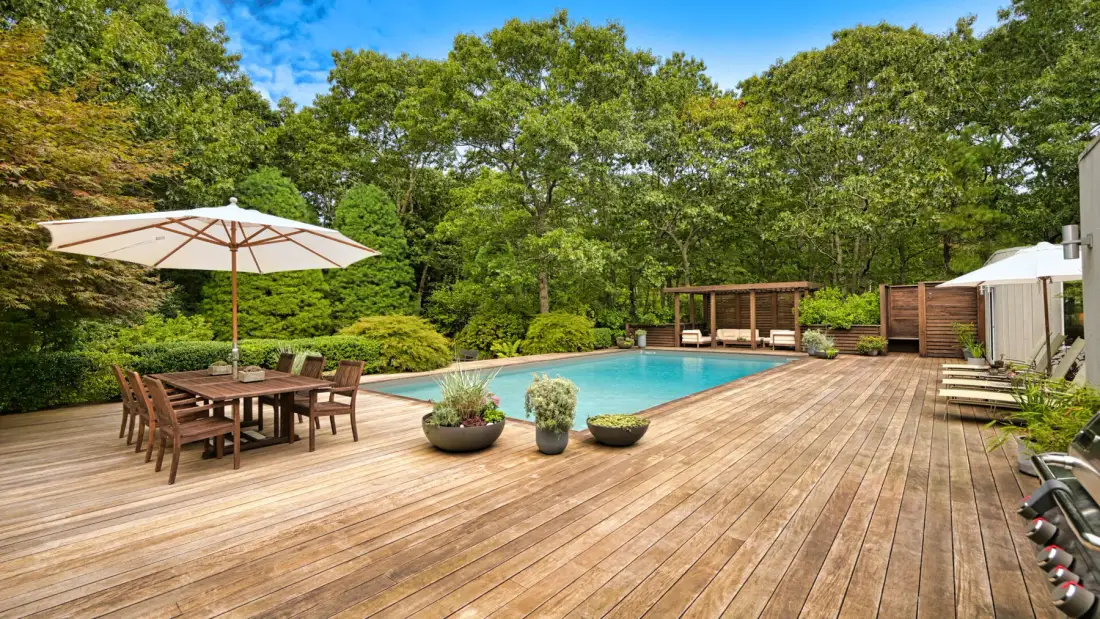 An outdoor swimming pool beside a spacious wooden deck and dining area.