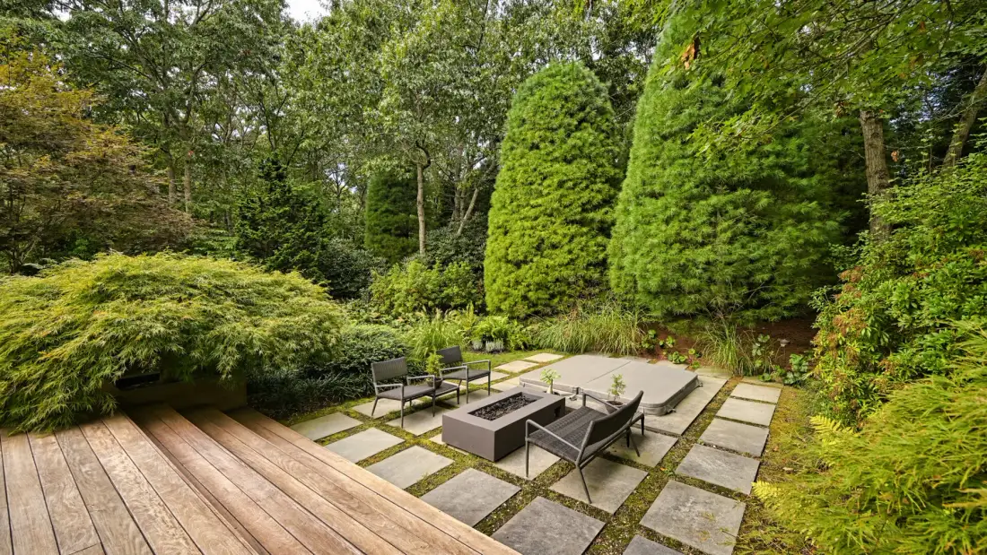 Un patio ajardinado con asientos al aire libre, losas y vegetación alrededor.