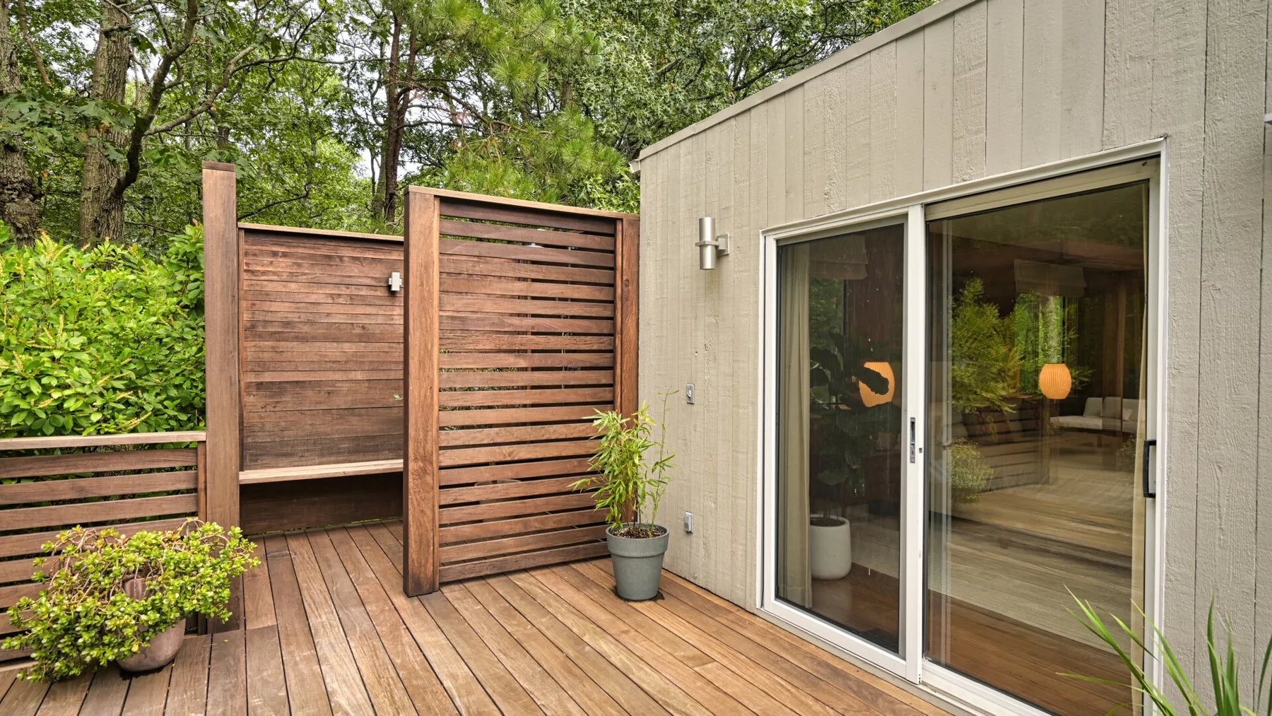 Una terraza de madera junto a un patio cercado y una puerta corrediza de vidrio.