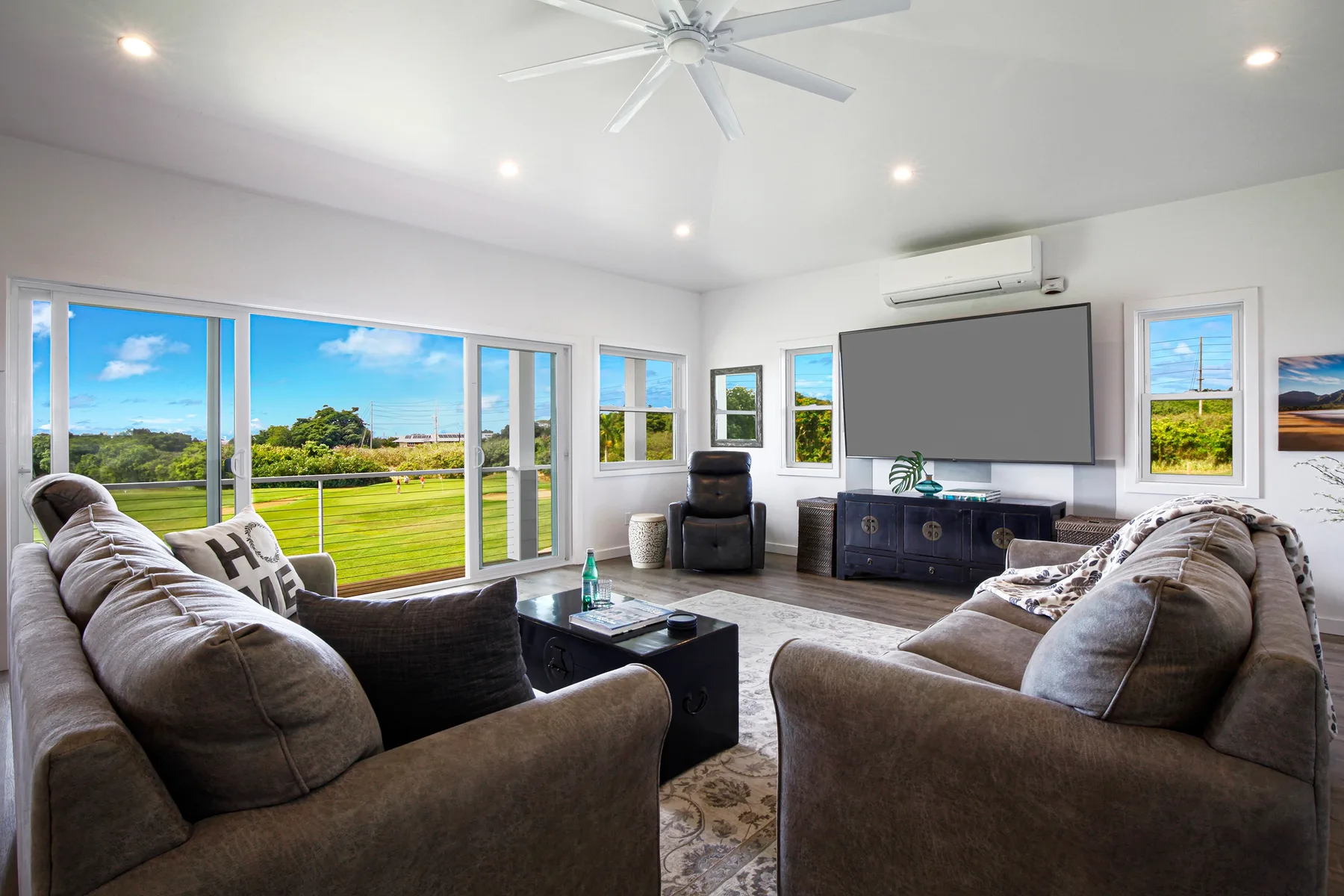 A bright living room with seating facing a large wall-mounted screen.