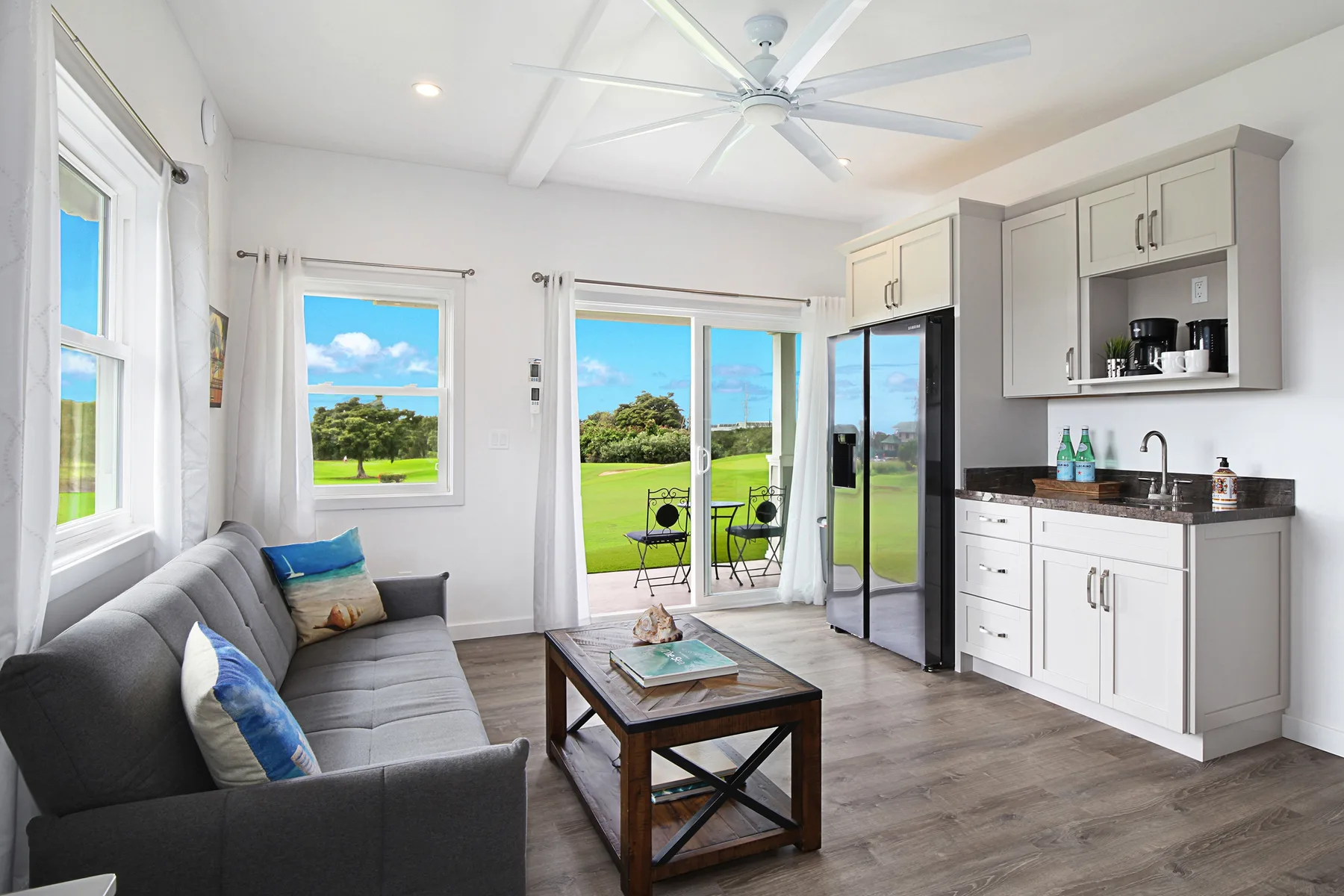A bright living area with a gray sofa, a small table, and a compact kitchen.