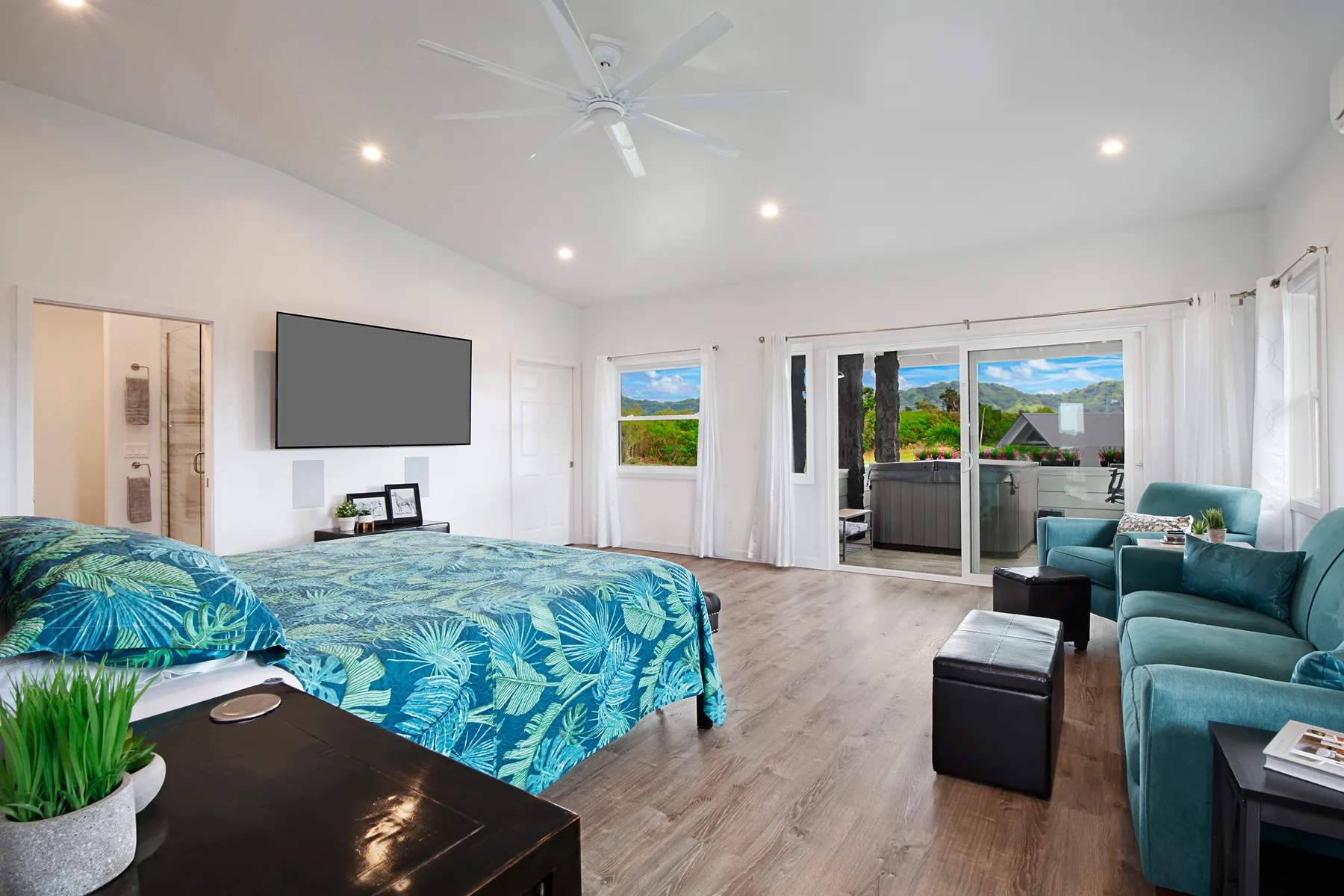 A bright bedroom with a patterned bedspread, television, and seating beside glass doors.
