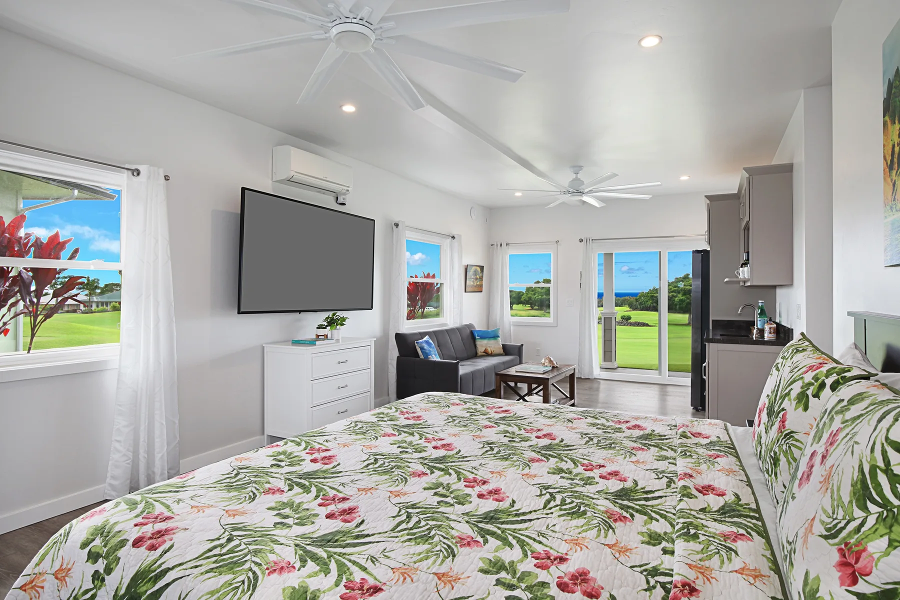A bright bedroom with a floral bed, seating area, and sliding glass doors.