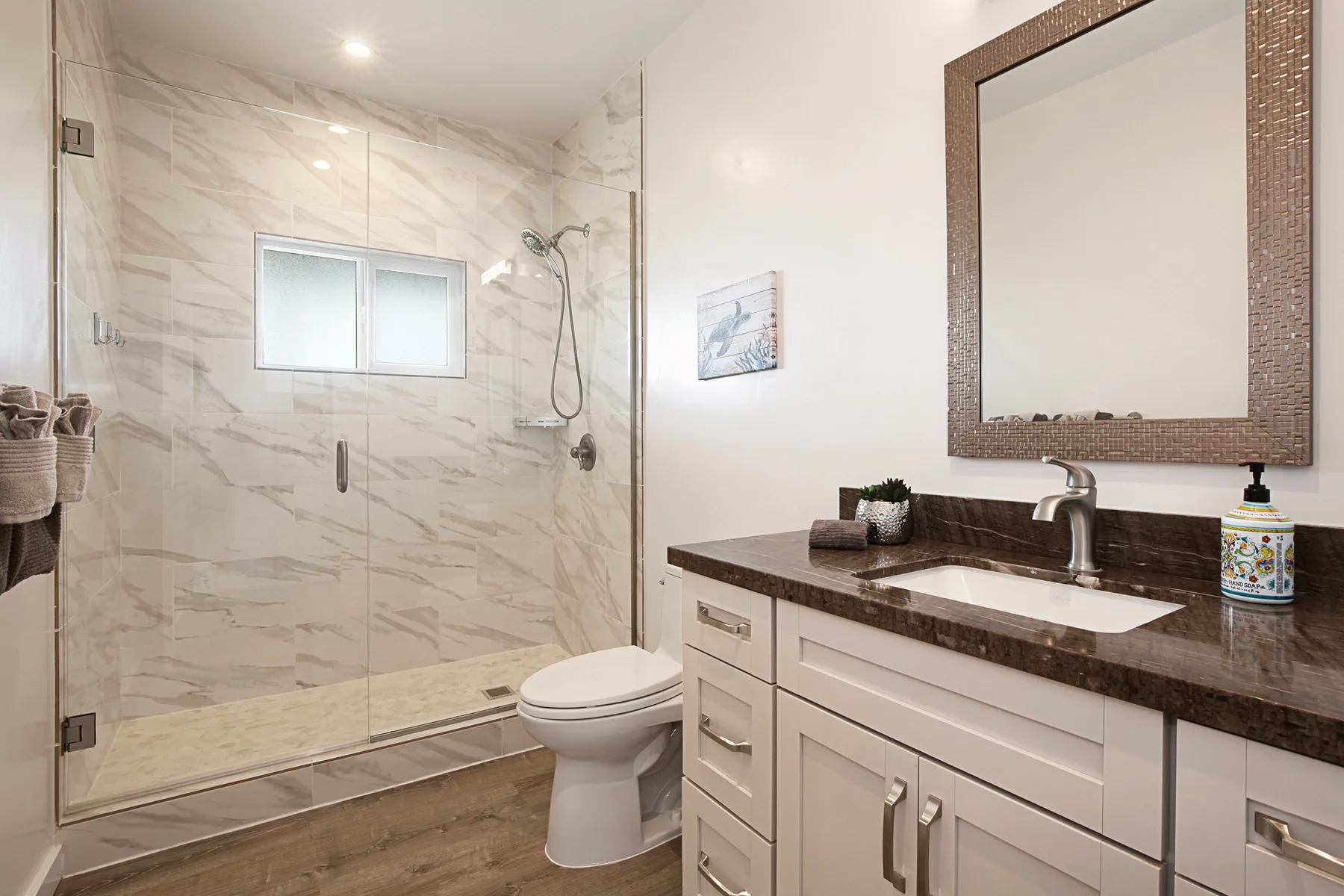 A bright bathroom with a glass shower, toilet, and vanity.