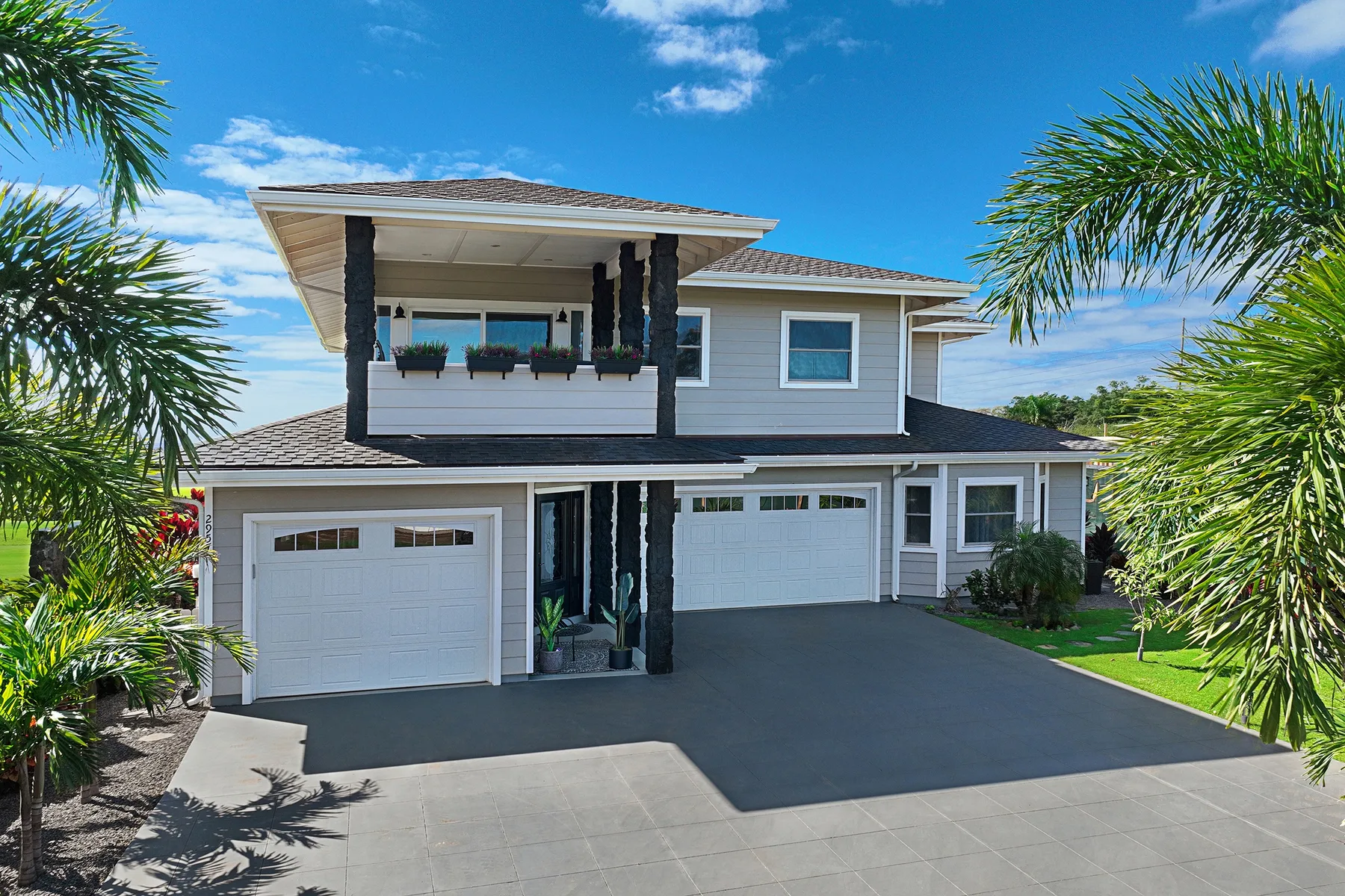A large gray house with white garage doors and palm trees in front.